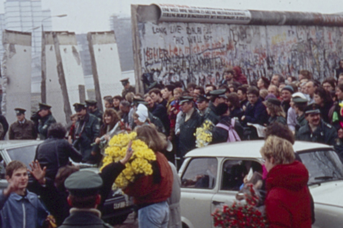 Menschenmenge und ein Trabant vor der durchbrochenen Mauer